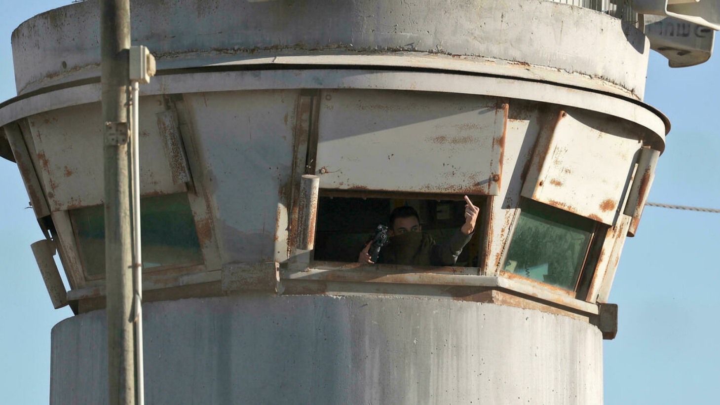 جندي إسرائيلي يلوح بيده من داخل غرفة برج للمراقبة عند معتقل عوفر قرب مدينة رام الله في الضفة الغربية المحتلة