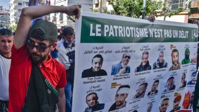 متظاهرون يحملون لافتة عليها صور معتقلي رأي في السجون الجزائرية