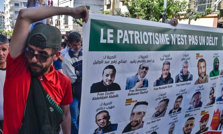 متظاهرون يحملون لافتة عليها صور معتقلي رأي في السجون الجزائرية